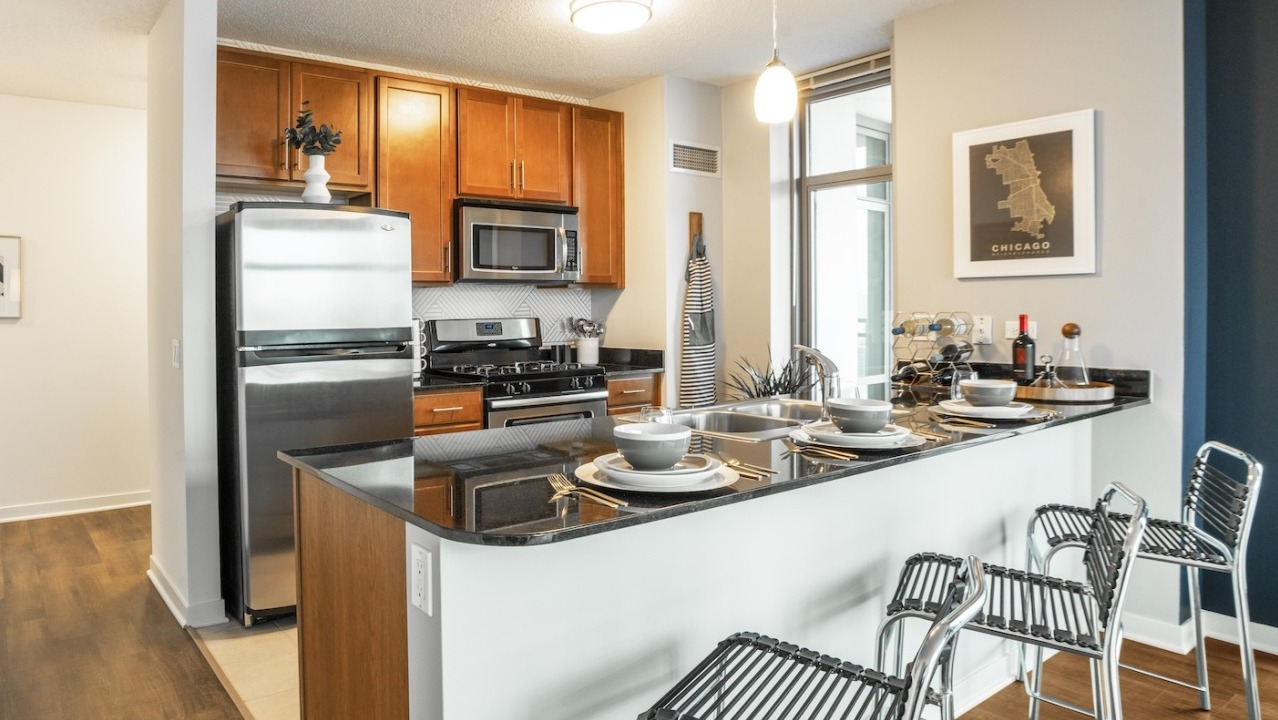Modern kitchen at Alta at K Station with stainless steel appliances, wood cabinetry, granite countertops, and breakfast bar seating