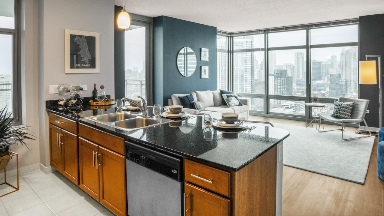 Open-concept kitchen at Alta at K Station featuring a granite island with sink, tile flooring, and sightlines to a bright living area with city views