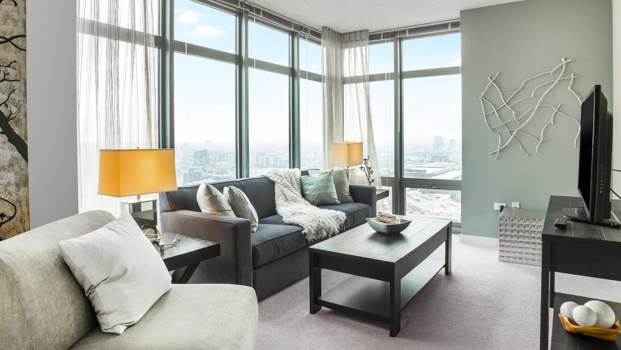 Cozy living area at Alta at K Station featuring floor-to-ceiling windows, modern sofa, twin table lamps, and soft décor for relaxed city living