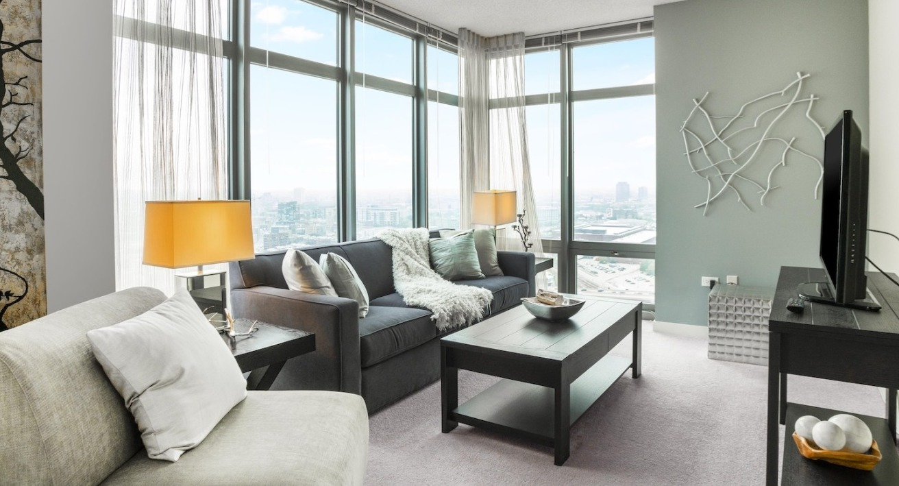 Cozy living area at Alta at K Station featuring floor-to-ceiling windows, modern sofa, twin table lamps, and soft décor for relaxed city living