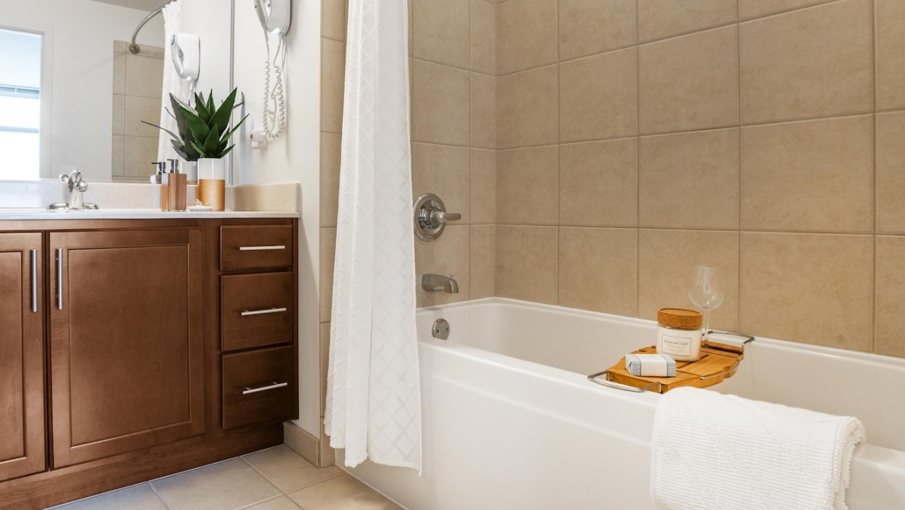 Master bathroom at Alta at K Station featuring tiled bathtub, wood cabinetry, wide vanity mirror, and neutral finishes for a spa-like design