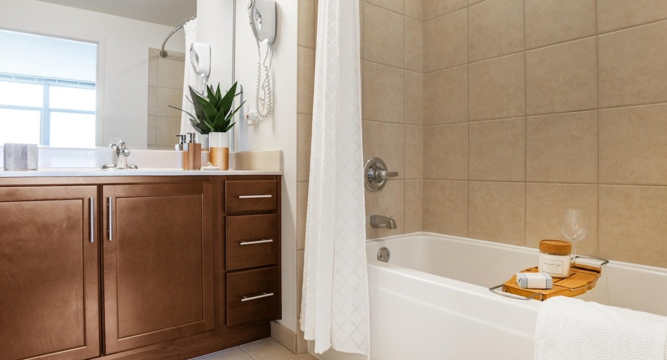 Master bathroom at Alta at K Station featuring tiled bathtub, wood cabinetry, wide vanity mirror, and neutral finishes for a spa-like design