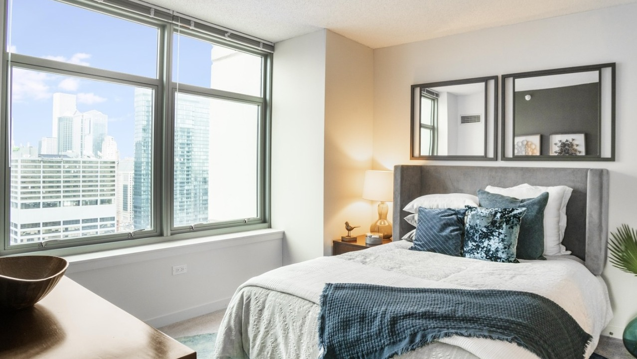 Master bedroom at Alta at K Station in Chicago with large windows, upholstered bed, soft bedding, and skyline views for a sophisticated retreat