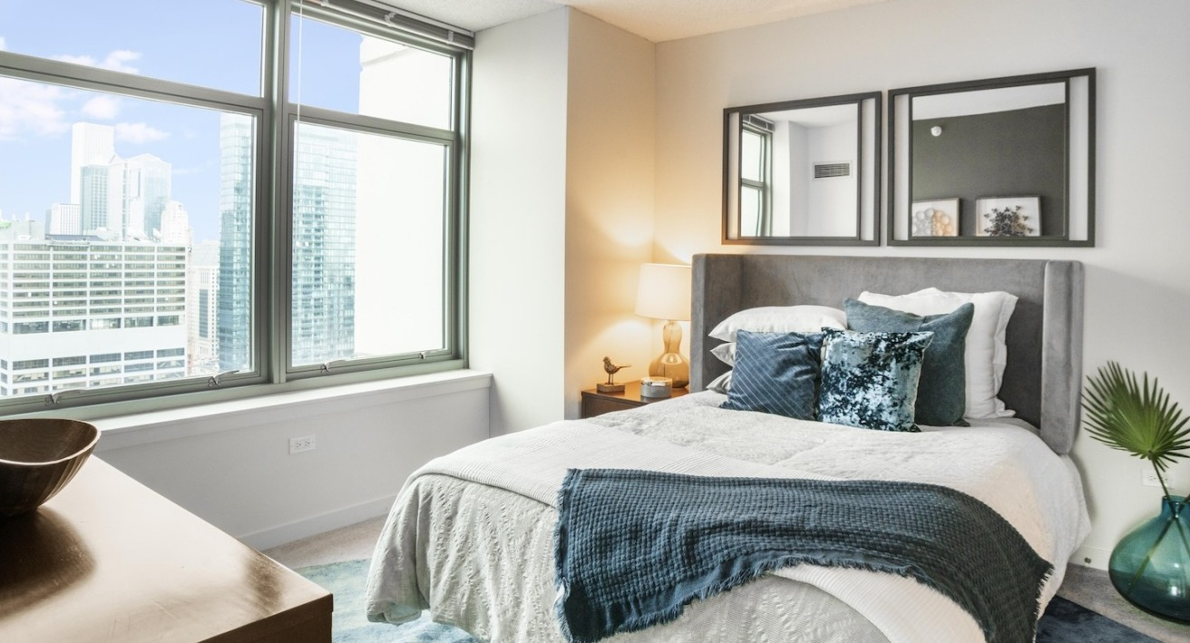 Master bedroom at Alta at K Station in Chicago with large windows, upholstered bed, soft bedding, and skyline views for a sophisticated retreat