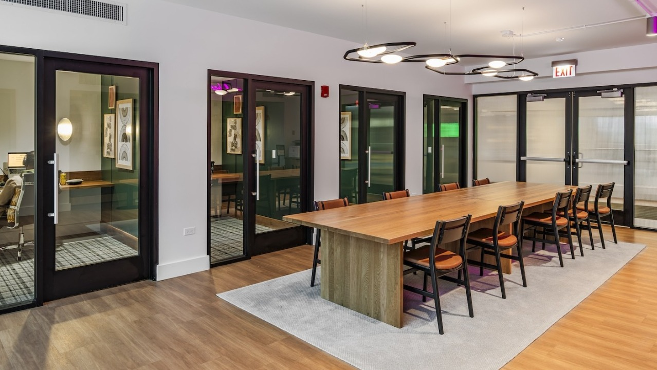 Spacious coworking space at Alta at K Station with a large wood table, private offices, and modern lighting for flexible resident work options