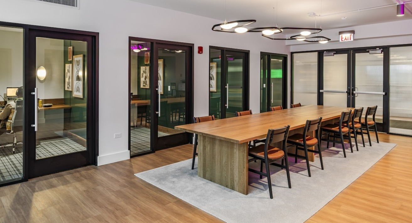 Spacious coworking space at Alta at K Station with a large wood table, private offices, and modern lighting for flexible resident work options