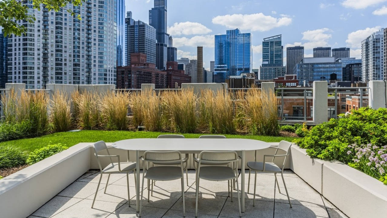 Outdoor dining area with table and chairs on the rooftop at Alta at K Station, surrounded by greenery and views of downtown Chicago skyscrapers