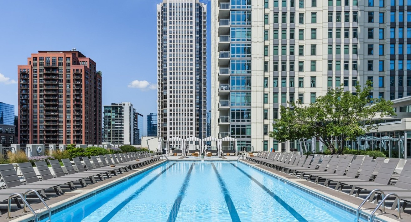 Rooftop swimming pool at Alta at K Station surrounded by lounge chairs, with panoramic views of Chicago high-rises and blue summer skies