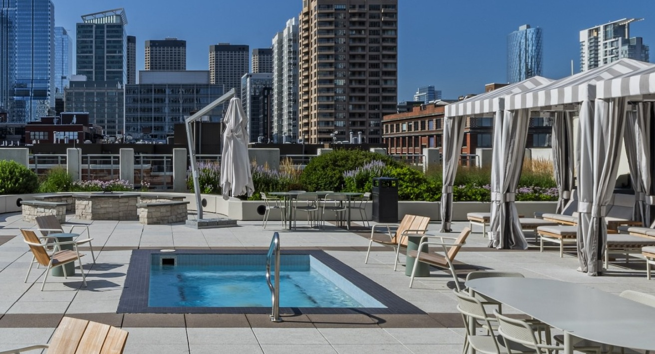 Expansive rooftop sundeck at Alta at K Station featuring a hot tub, shaded cabanas, fire pit, and outdoor dining areas overlooking downtown Chicago