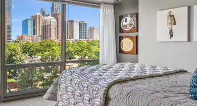Bright bedroom at AMLI 900 with floor-to-ceiling windows overlooking Chicago’s skyline, layered bedding, nightstand lamp, and contemporary wall art