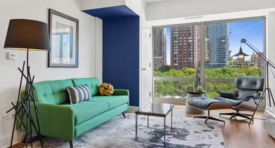 Bright living room at AMLI 900 with green sofa, lounge chair, large windows, skyline views, and bold accent walls for modern Chicago apartment living