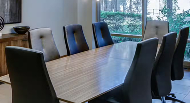 Modern conference room at AMLI 900 featuring a long wood table, high-back chairs, art and credenza, pendant lights, and a window with greenery in Chicago