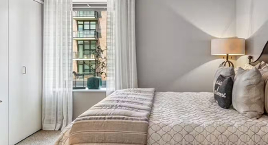 Cozy bedroom at AMLI 900 with upholstered headboard, layered bedding, large closet doors, soft lamp lighting, and a bright window with daylight in Chicago