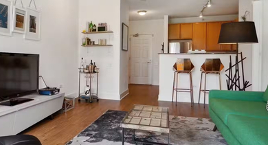 Cozy living room at AMLI 900 with green sofa, media console, wall art, and an open kitchen with bar seating, ideal for relaxed city living in Chicago