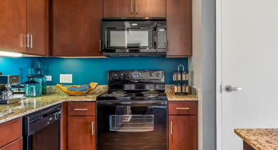 Stylish kitchen at AMLI 900 with granite countertops, warm wood cabinets, teal backsplash, and black appliances, opening toward the dining area in Chicago