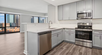 Open-layout kitchen and living room at AMLI 900 with granite island, pendant lighting, teal accents, and floor-to-ceiling windows showcasing Chicago city views