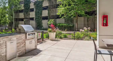 Shaded outdoor grilling station at AMLI 900 featuring stainless BBQs, prep counters, dining table, and a landscaped courtyard setting for summer cookouts in Chicago