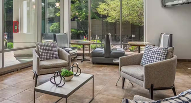 Light-filled resident lounge at AMLI 900 offering comfy chairs, café tables, TV, and expansive windows with views of the landscaped patio area in Chicago