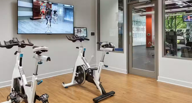 Spin studio at AMLI 900 with stationary bikes facing a large screen for virtual classes, wood floors, and glass doors connecting to the main gym in Chicago