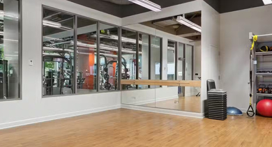 Fitness studio at AMLI 900 with mirrored wall and barre, TRX straps, kettlebells, stability balls, and hardwood floors for yoga and functional training in Chicago
