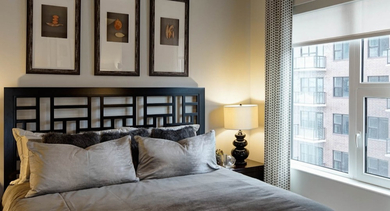 Cozy bedroom with a dark headboard, soft bedding, and a large window offering city views at AMLI Lofts in Chicago
