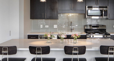 Modern kitchen with dark cabinetry, stainless steel appliances, and a large island with four bar stools at AMLI Lofts