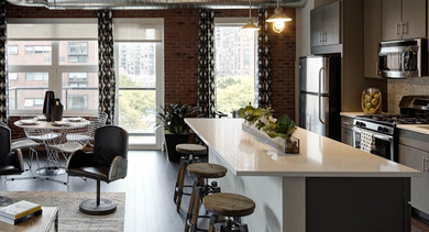 Open-concept living room and kitchen area with exposed brick, large windows, and modern finishes at AMLI Lofts in Chicago