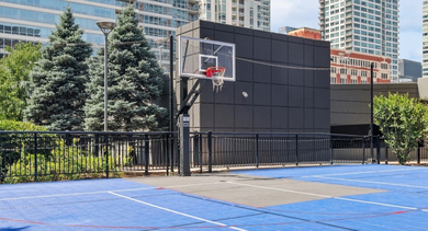 Bright blue outdoor basketball court surrounded by greenery and city buildings at AMLI Lofts in Chicago