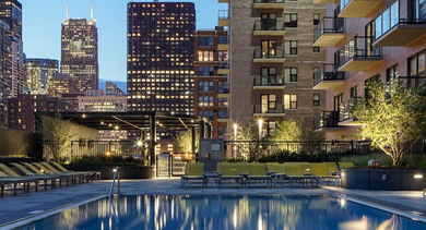 Outdoor swimming pool area illuminated at night, showcasing lounge chairs and city skyline views at AMLI Lofts in Chicago