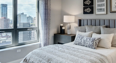 Cozy bedroom at AMLI River North, featuring plush bedding, stylish decor, and a large window with city views