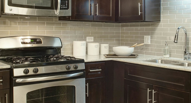 Gourmet kitchen at AMLI River North, boasting dark wood cabinets, stainless steel appliances, and sleek grey subway tile backsplash