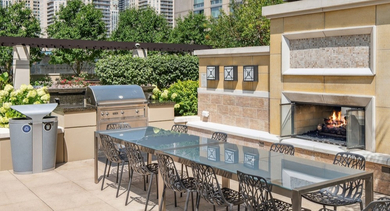 Outdoor patio at AMLI River North, featuring a grilling station, a large dining table, and a cozy outdoor fireplace