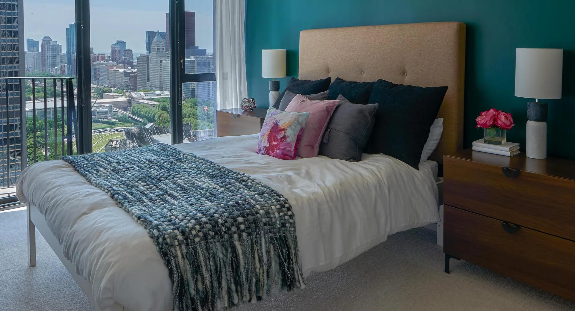 Stylish bedroom with emerald feature wall, upholstered headboard, nightstands, and sweeping Chicago skyline views at Aqua at Lakeshore East Apartments