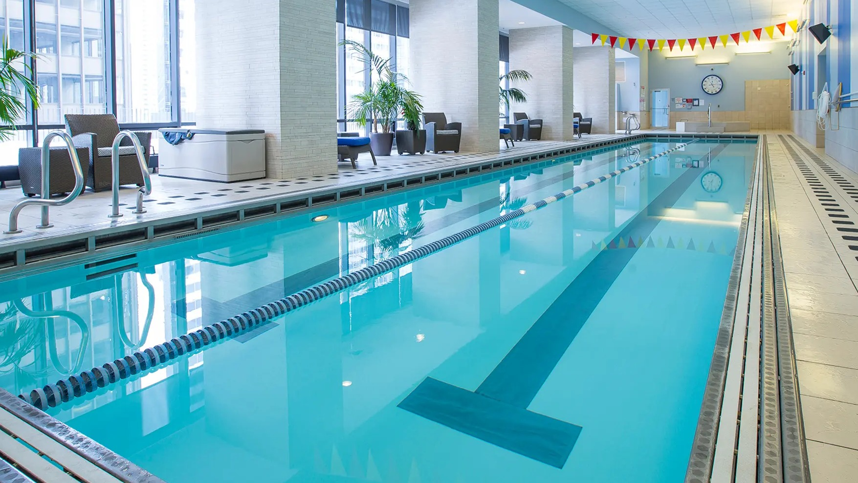 Indoor lap pool with lane markers, modern seating, and large windows offering city views at Aqua at Lakeshore East Apartments in Chicago
