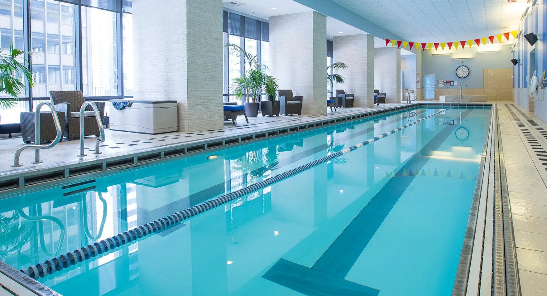 Indoor lap pool with lane markers, modern seating, and large windows offering city views at Aqua at Lakeshore East Apartments in Chicago