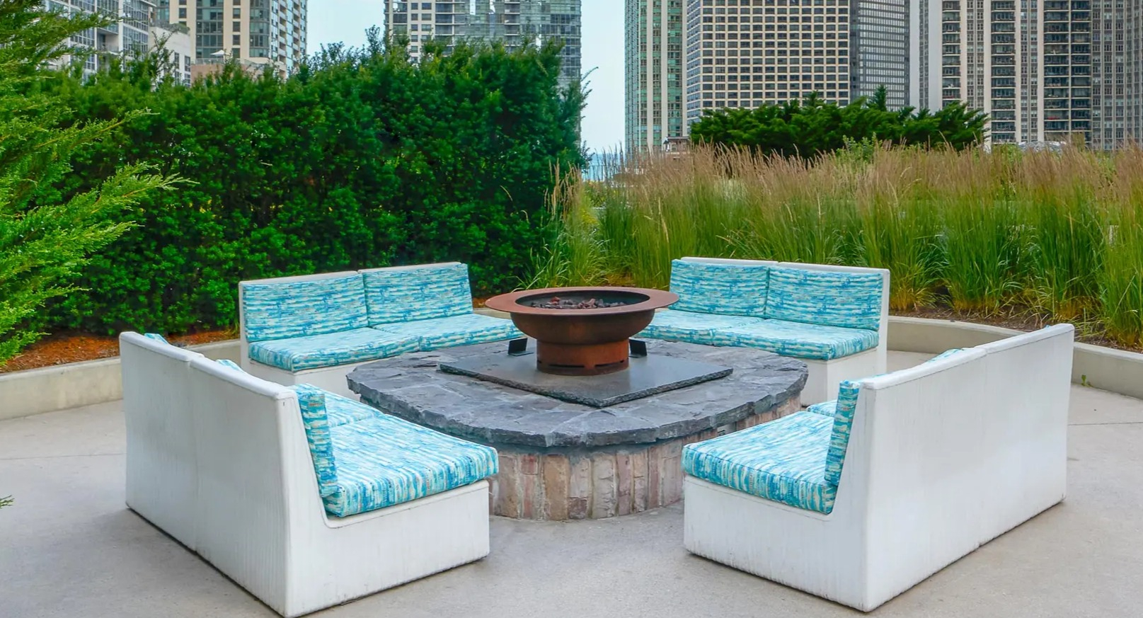 Outdoor fire pit lounge with modern seating, city high-rise views, and lush greenery at Aqua at Lakeshore East Apartments in Chicago