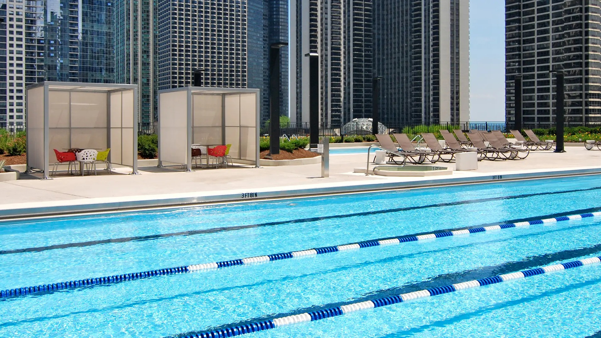 Outdoor pool deck with lap lanes, cabanas, and lounge chairs set against Chicago high-rises at Aqua at Lakeshore East Apartments in Lakeshore East