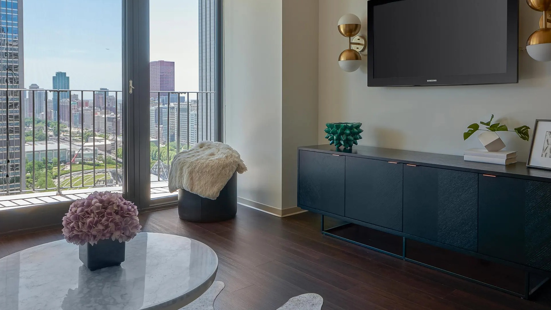 Chic living room with media console, wall-mounted TV, and balcony overlooking Chicago parks and towers at Aqua at Lakeshore East Apartments