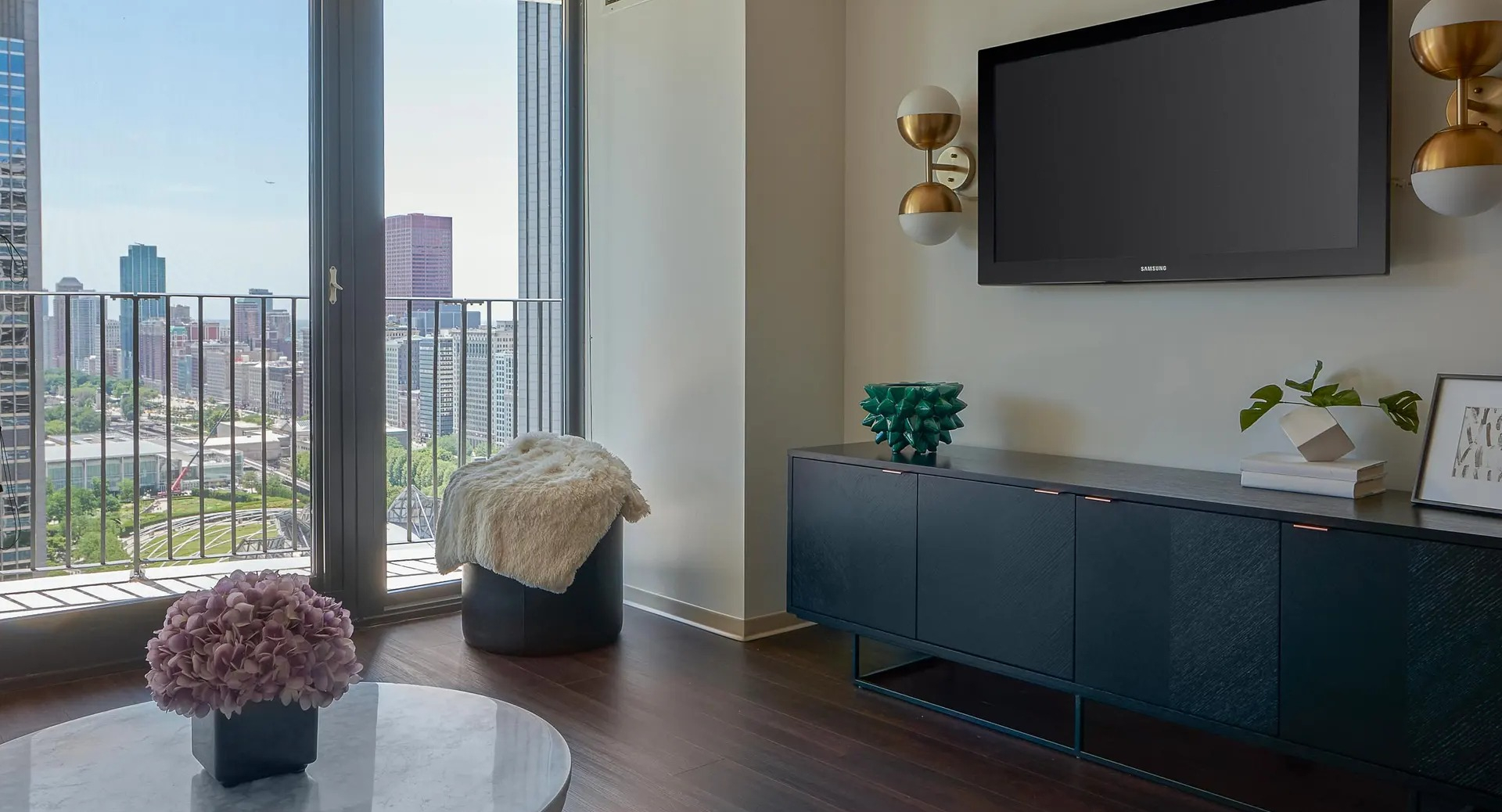 Chic living room with media console, wall-mounted TV, and balcony overlooking Chicago parks and towers at Aqua at Lakeshore East Apartments