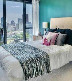 Stylish bedroom with a bold green accent wall, modern furniture, and floor-to-ceiling windows with city views at Aqua at Lakeshore East