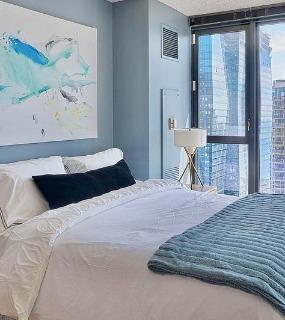 Modern bedroom with a cozy bed, abstract artwork, and floor-to-ceiling windows offering stunning city and lake views at Aqua at Lakeshore East