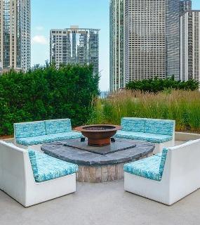 Outdoor seating area with a firepit surrounded by lush greenery and city skyline views at Aqua at Lakeshore East