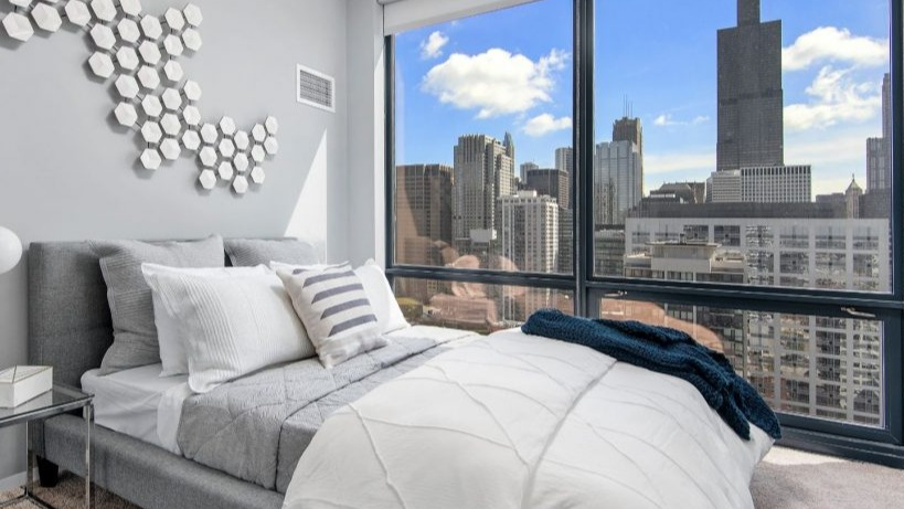 Cozy bedroom at Arkadia West Loop with a comfy bed, modern wall art, and a striking cityscape view