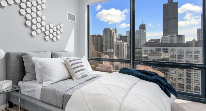 Cozy bedroom at Arkadia West Loop with a comfy bed, modern wall art, and a striking cityscape view