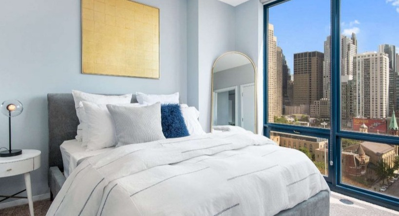Cozy bedroom at Arkadia West Loop featuring a comfortable bed, stylish decor, and stunning city views
