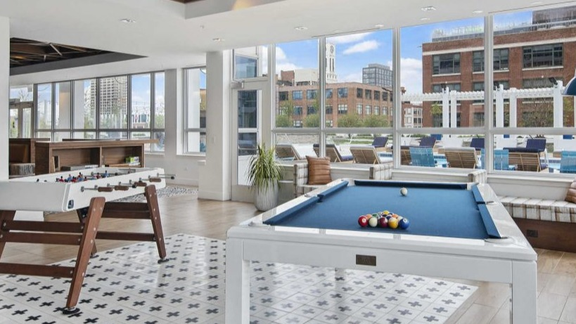 Engaging game room at Arkadia West Loop with a pool table, foosball, and large windows with city views