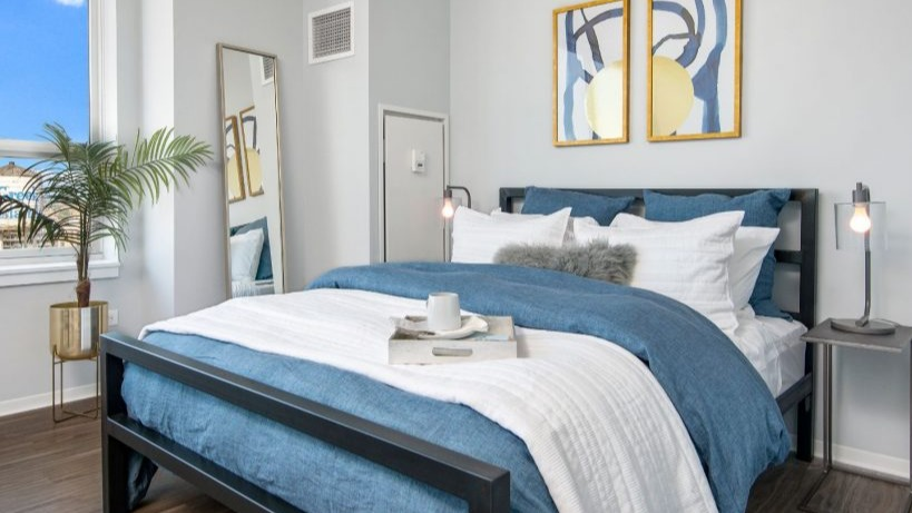 Modern bedroom at Arkadia West Loop with a dark frame bed, blue bedding, and a bright window with city views