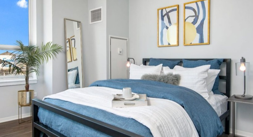 Modern bedroom at Arkadia West Loop with a dark frame bed, blue bedding, and a bright window with city views