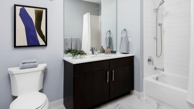 Sleek bathroom at Arkadia West Loop featuring a dark wood vanity, white tiles, and modern artistic decor