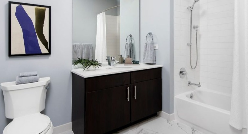 Sleek bathroom at Arkadia West Loop featuring a dark wood vanity, white tiles, and modern artistic decor